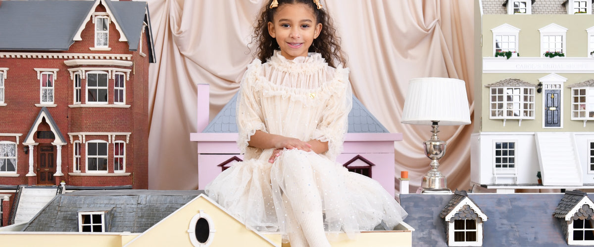 Twee meisjes in ivoren feestjurken van Angel's Face tussen poppenhuizen – designer kinderkleding | Niñoz Almere