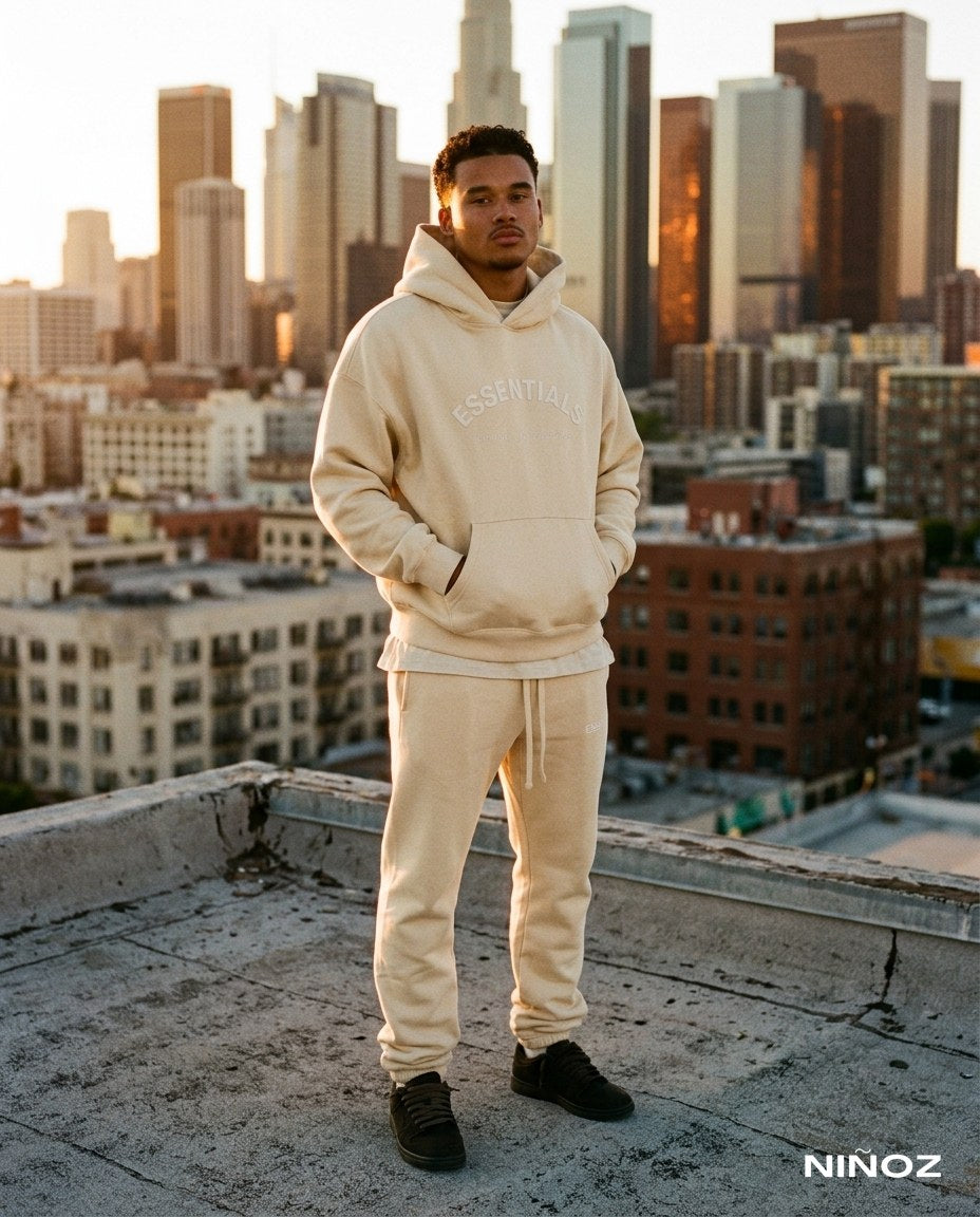 Essentials Cou7ure heren — beige tracksuit met hoodie, skyline op de achtergrond, bij Niñoz