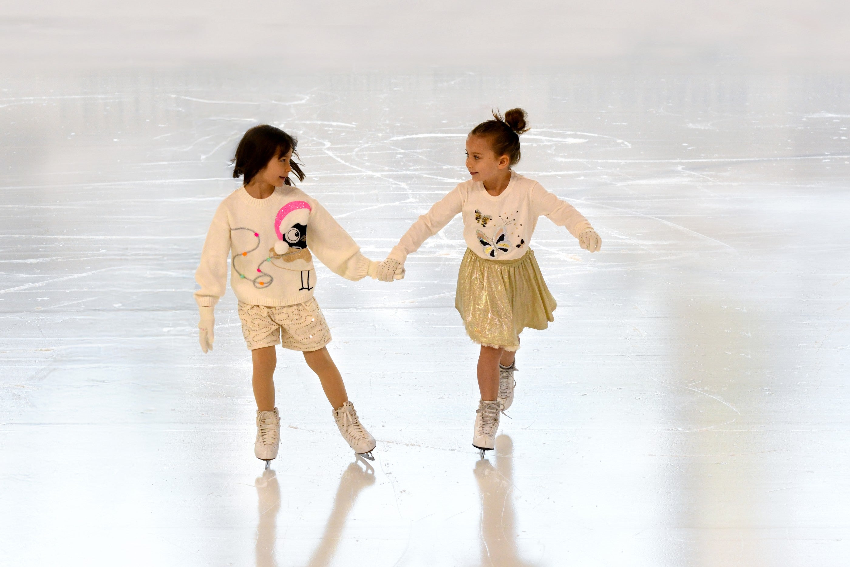 Twee meisjes schaatsen hand in hand in Billieblush winterkleding — Billieblush wintercollectie 2026 bij Niñoz Almere