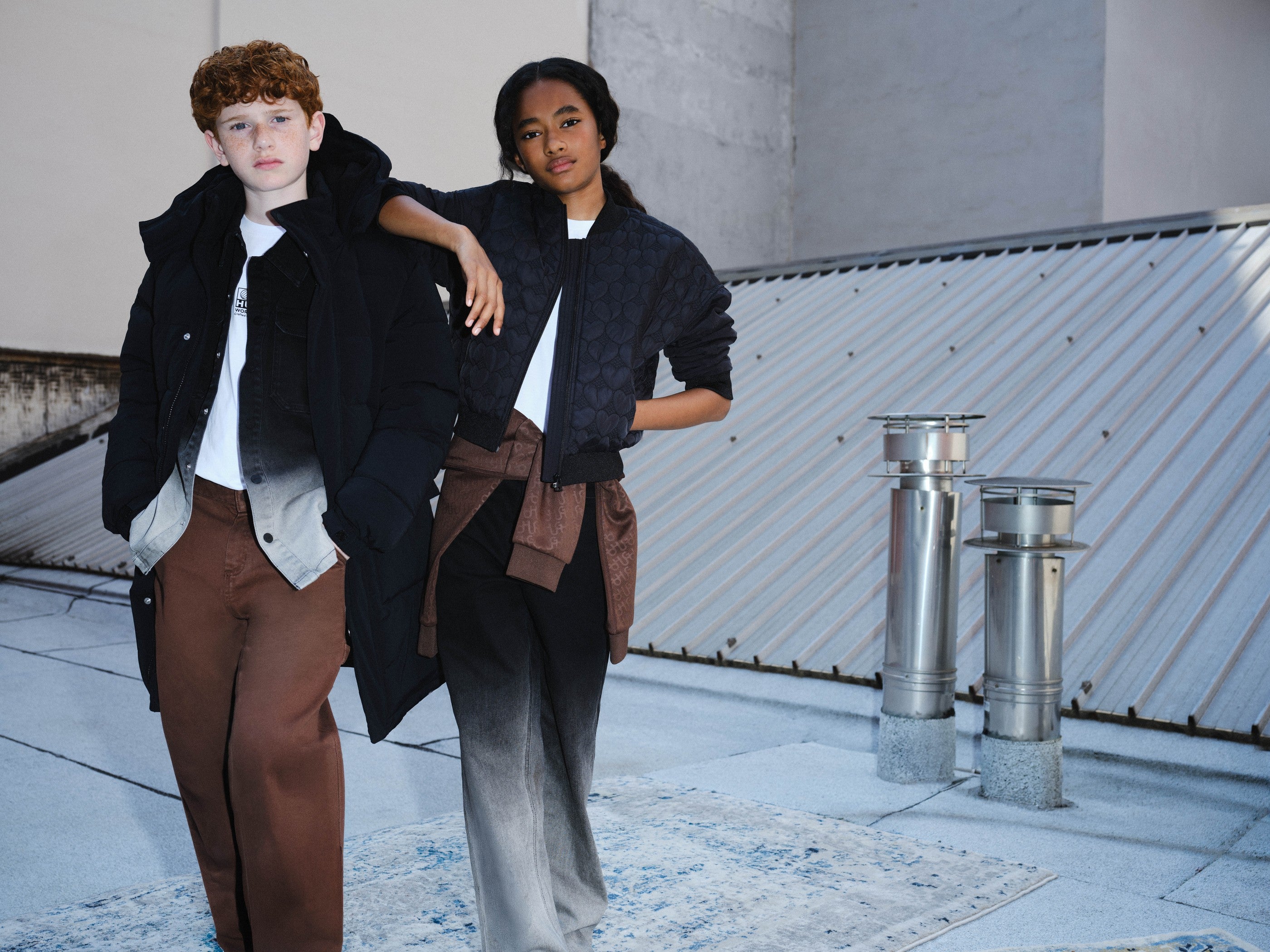 Twee tieners in HUGO winterjassen op een dak — HUGO kinderkleding wintercollectie 2026 bij Niñoz Almere