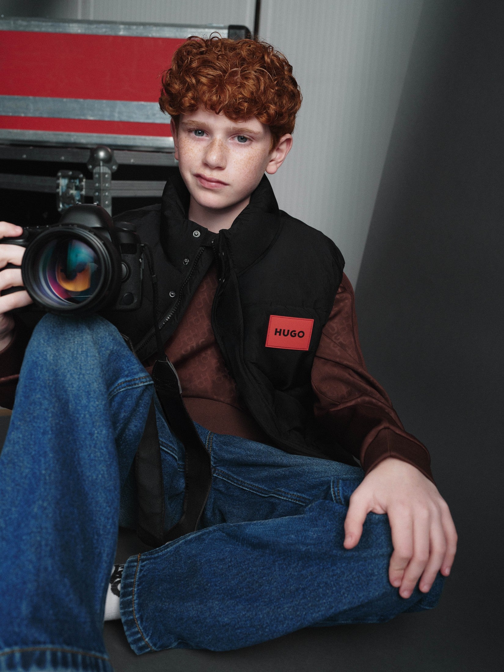 Jongen met camera in HUGO winterjas en spijkerbroek — jongenskleding winter 2026 bij Niñoz Almere