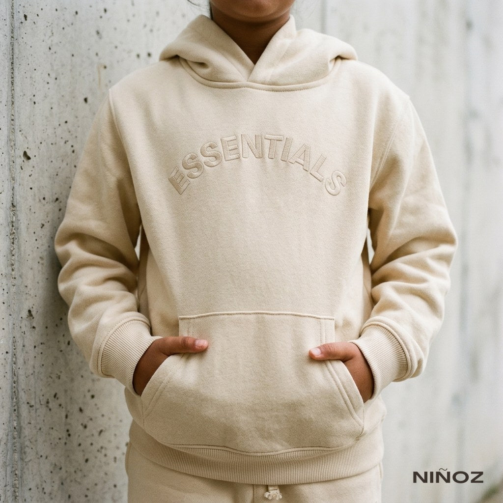 Close-up van de borstopdruk op een beige Essentials Cou7ure kinderhoodie — vakantiekleding voor je baby bij Niñoz