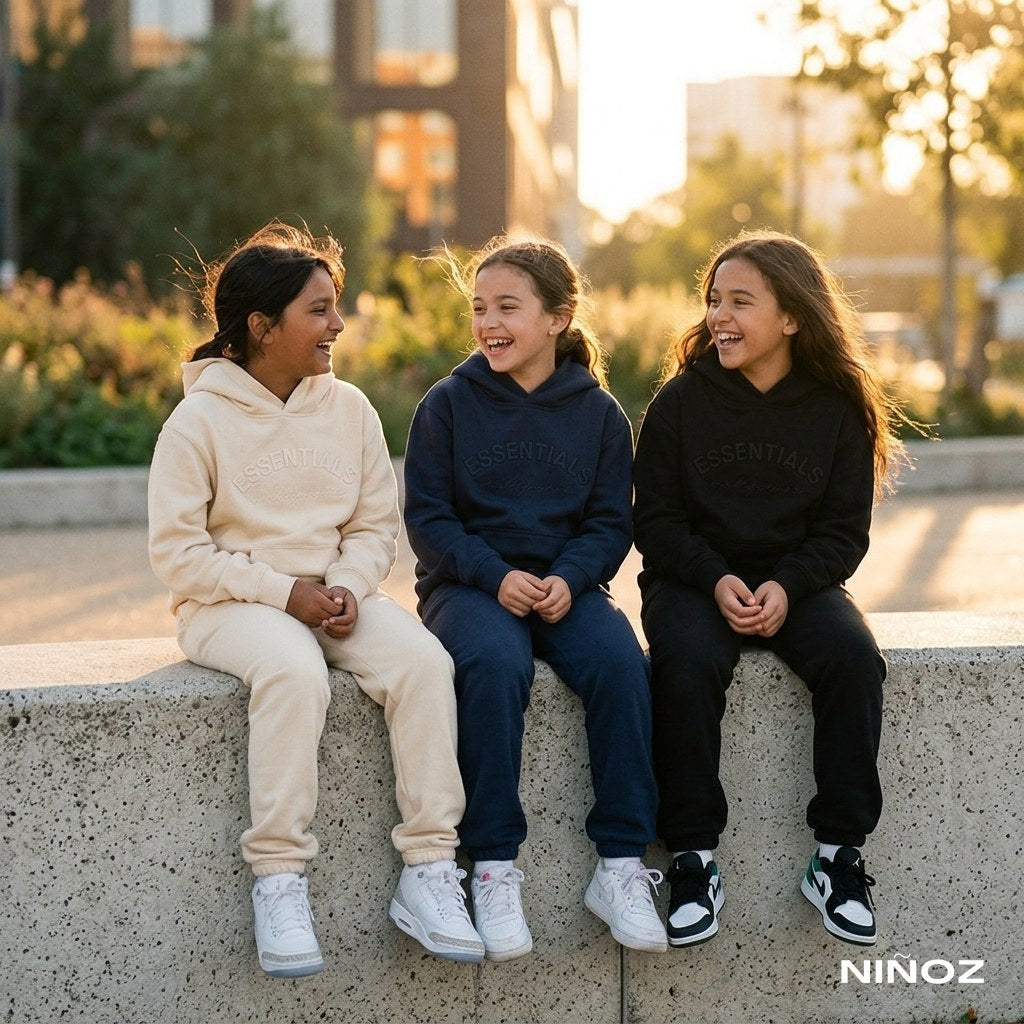 Drie meisjes in Essentials Cou7ure tracksuits bij een betonmuur — vakantiekleding voor meisjes bij Niñoz Almere