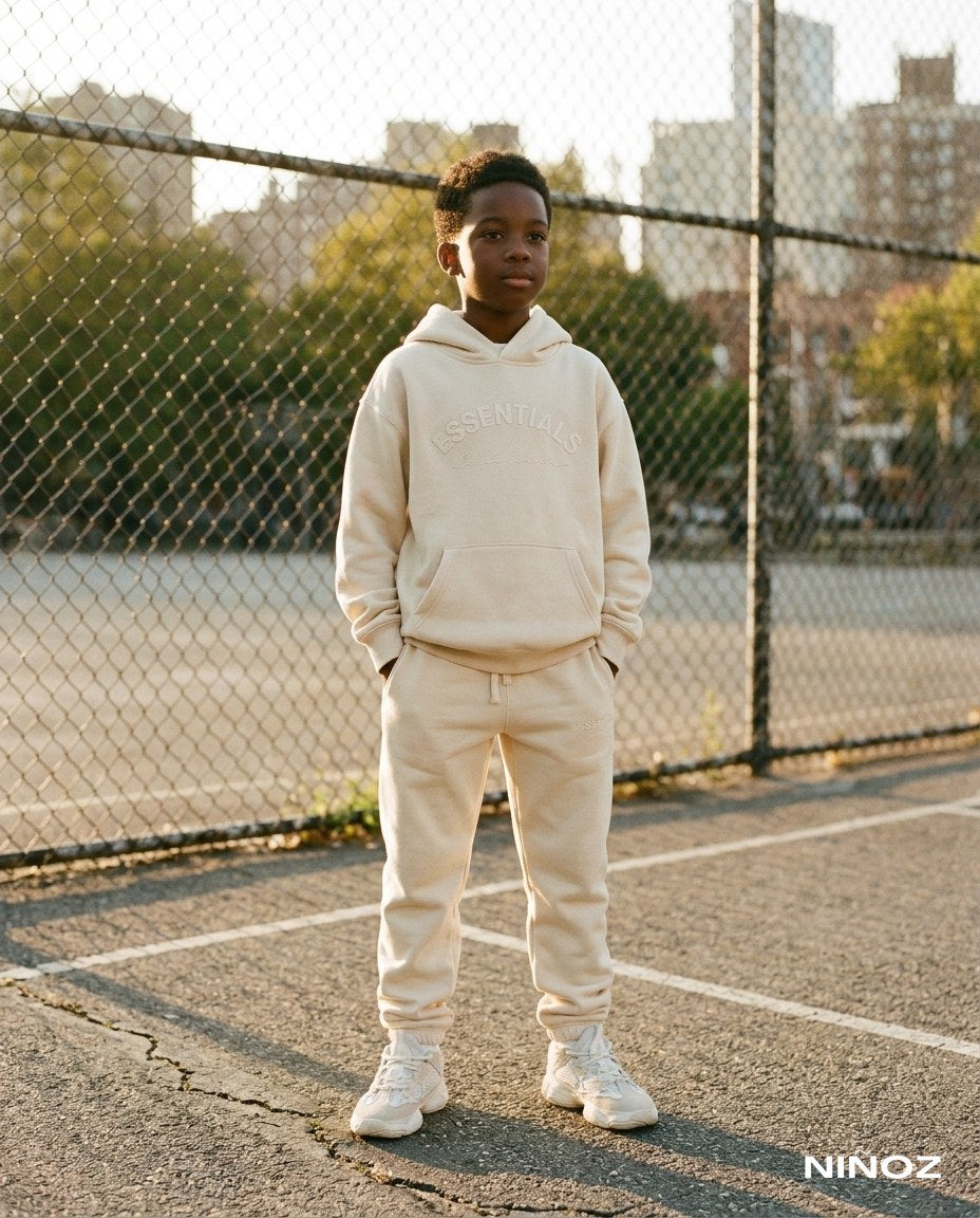 Jongen in beige Essentials Cou7ure tracksuit op een basketbalveld — sportieve kinderkleding bij Niñoz Almere