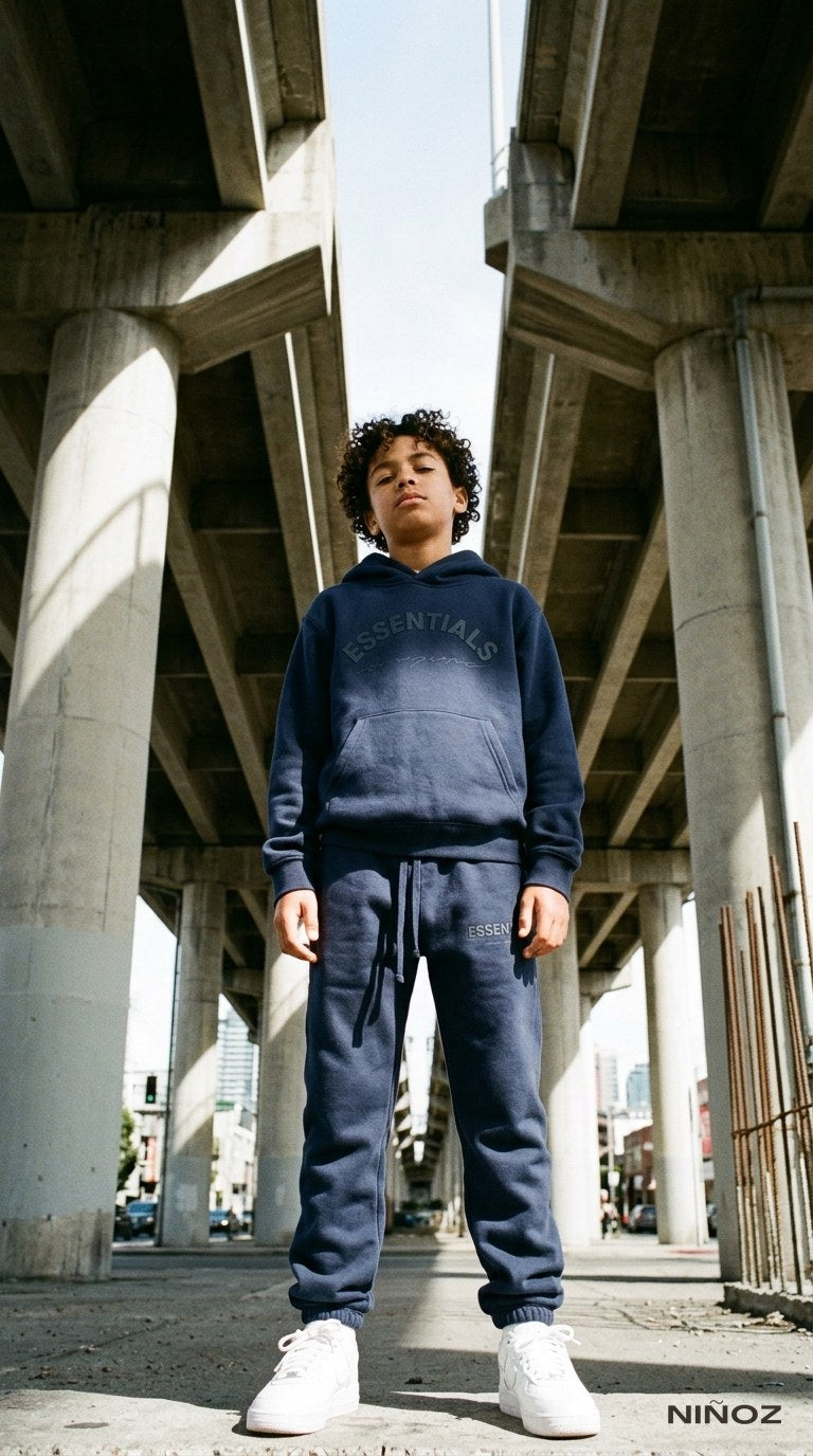 Jongen in navy Essentials Cou7ure tracksuit onder een viaduct — stoere kindermode bij Niñoz Almere