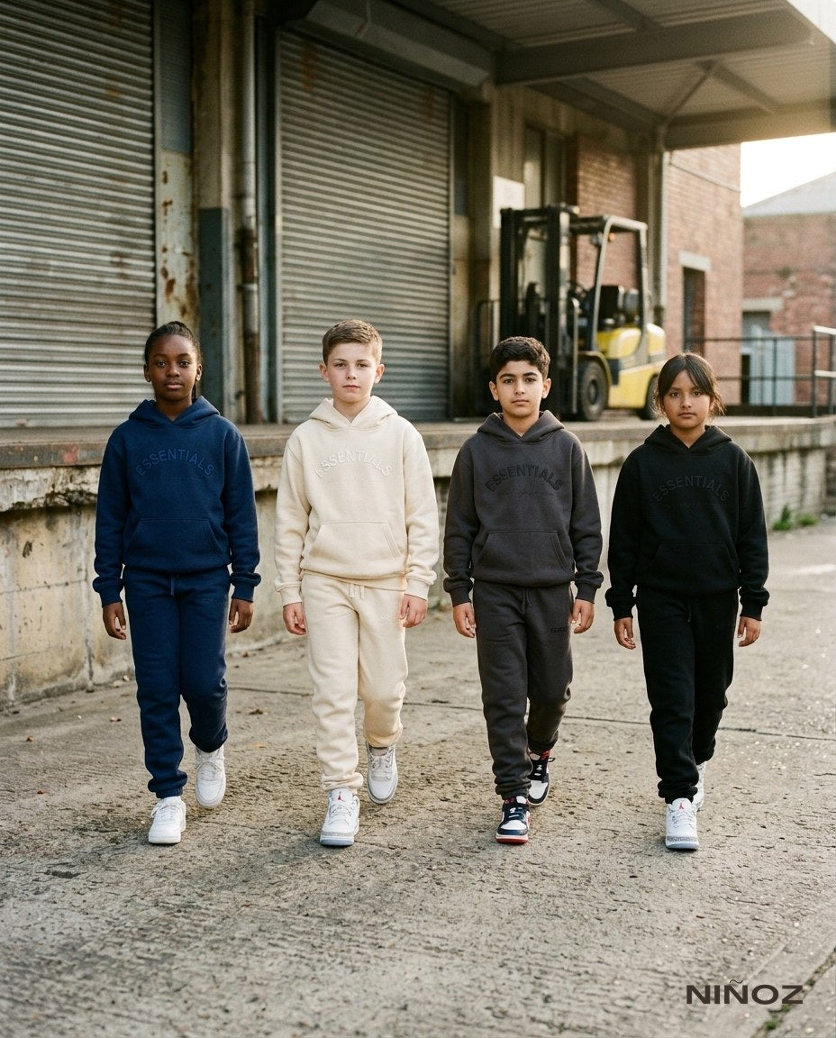 Vier kinderen in Essentials Cou7ure tracksuits lopen samen langs een laadperron — back-to-school kinderkleding bij Niñoz