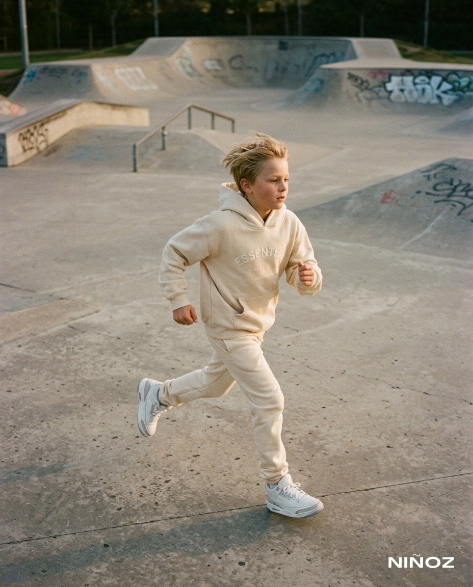 Jongen in beige Essentials Cou7ure tracksuit rent door een skatepark — Niñoz Almere