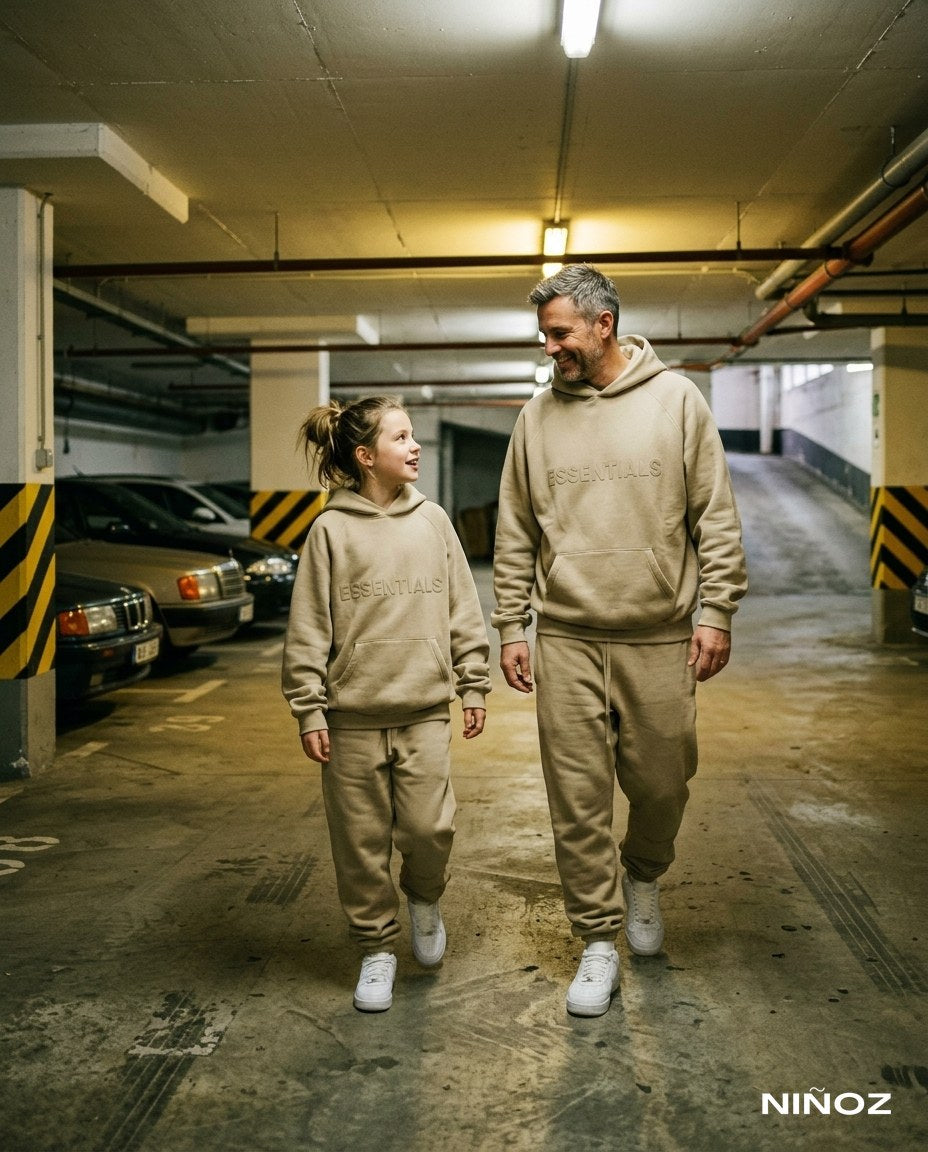 Vader en dochter in matching beige Essentials Cou7ure tracksuits in een parkeergarage — Niñoz Almere