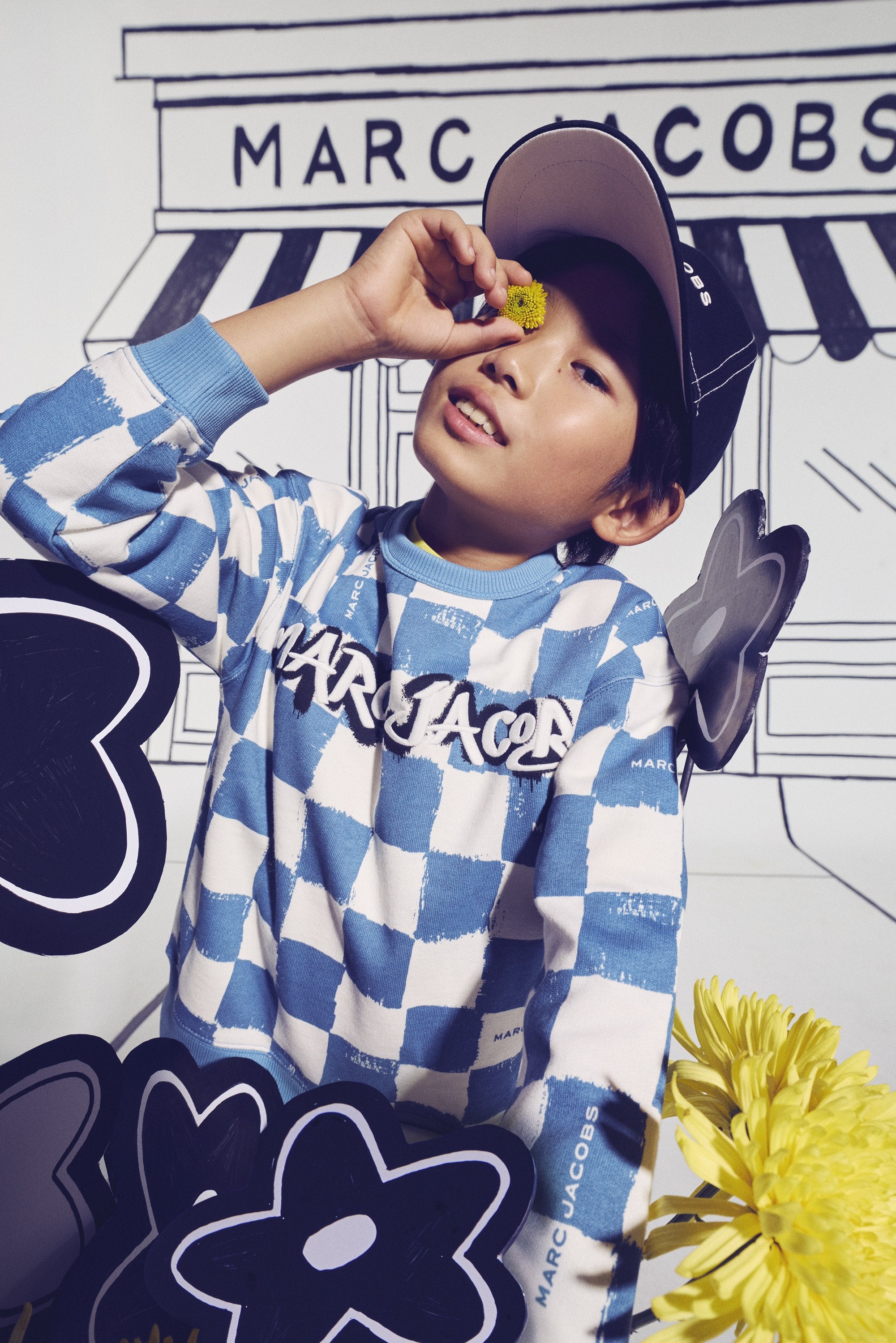 Jongen in geruite Marc Jacobs outfit voor een Marc Jacobs-winkelgevel — fashion-forward kindermode bij Niñoz